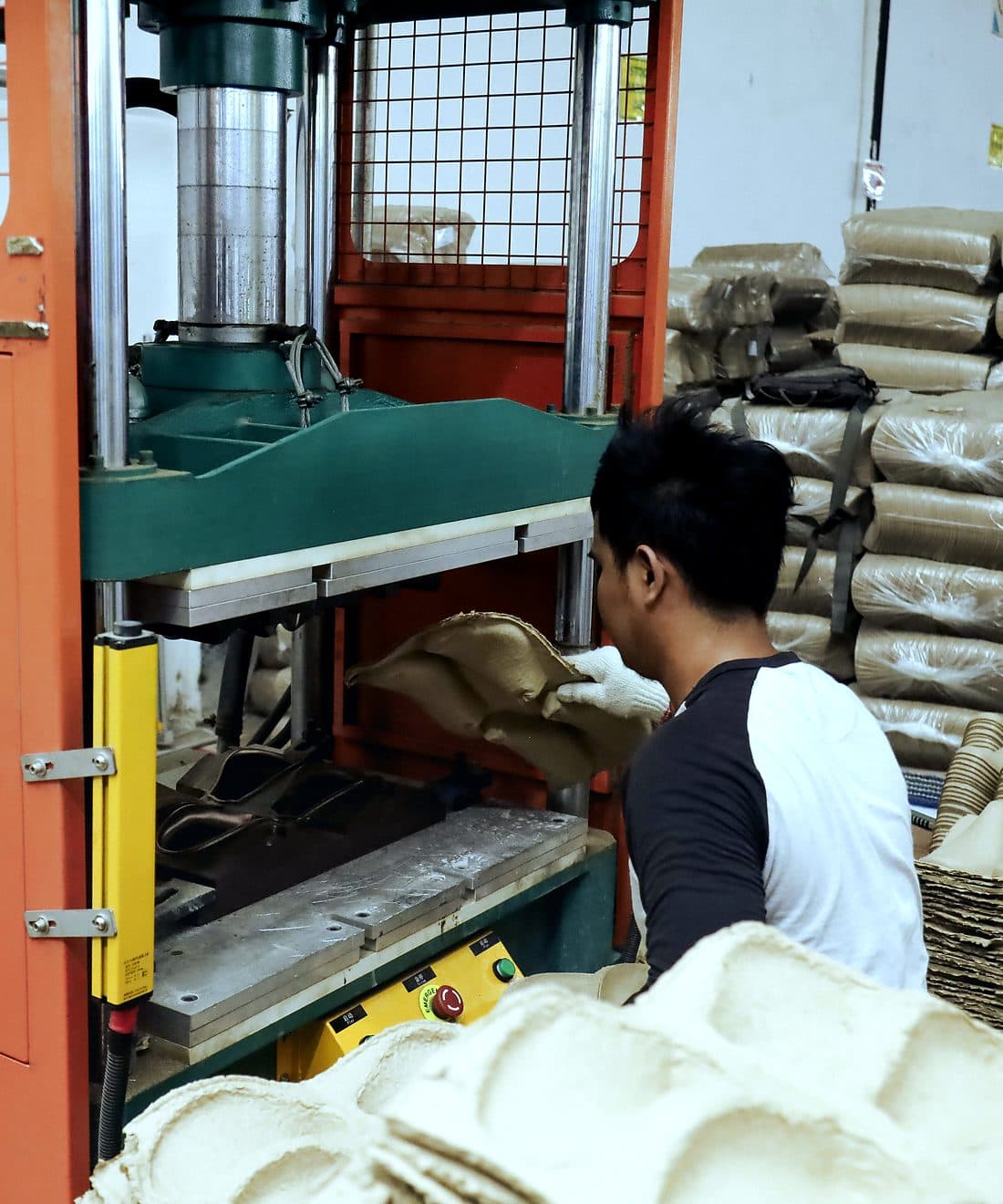 Operator mengangkat nampan pulp cetak dari mesin press di pabrik Karawang kami